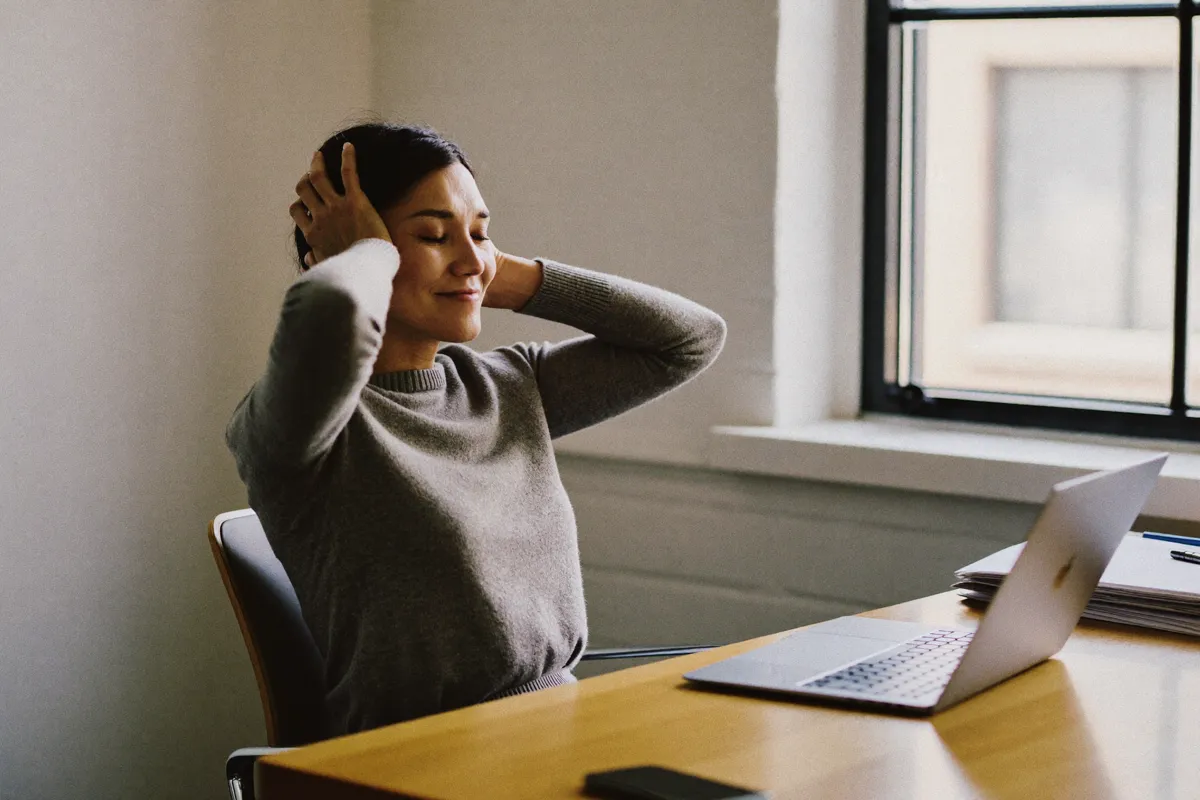 A woman leaning back from her desk with her eyes closed, visibly relieved